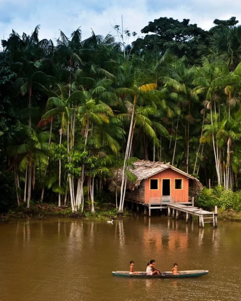 Traditional Amazonian riverside community with wooden stilt houses, canoes, and lush rainforest in the background.